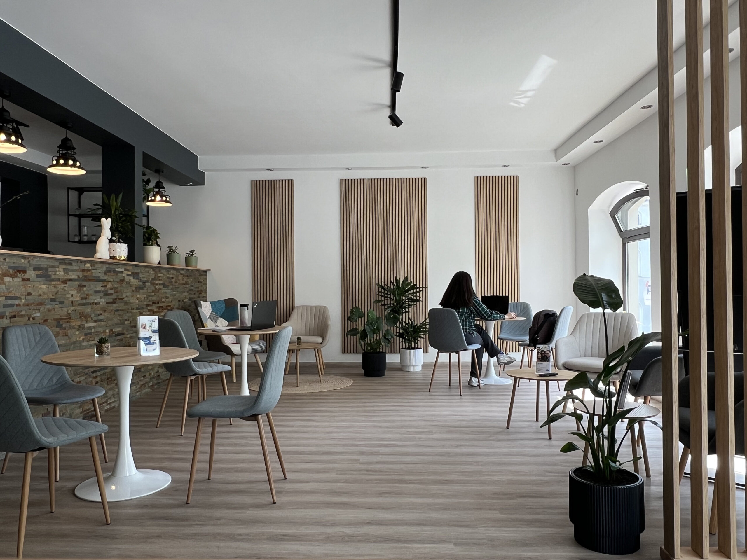 DigiUp Strausberg - Ein digitaler Ort für alle! - Modernes Raumkonzept, lichtdurchflutetes Begegnungs- und Lernraum mit stilvoller Einrichtung – Menschen sitzen an Tischen und arbeiten oder unterhalten sich