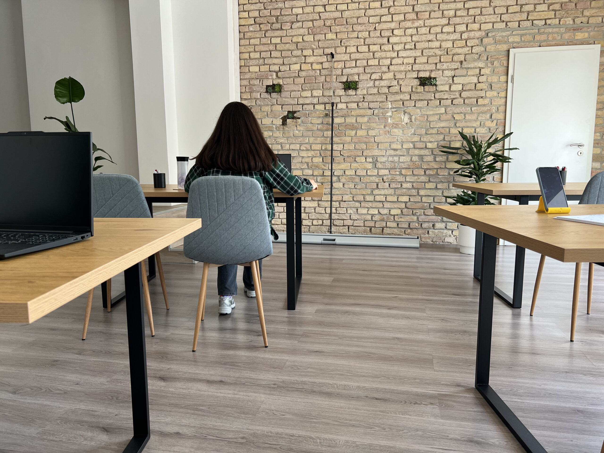 DigiUp Strausberg - Ein digitaler Ort für alle! -Teilnehmerin im DigiUp Strausberg beim Arbeiten im modernen Seminarraum mit Backsteinwand und Pflanzen