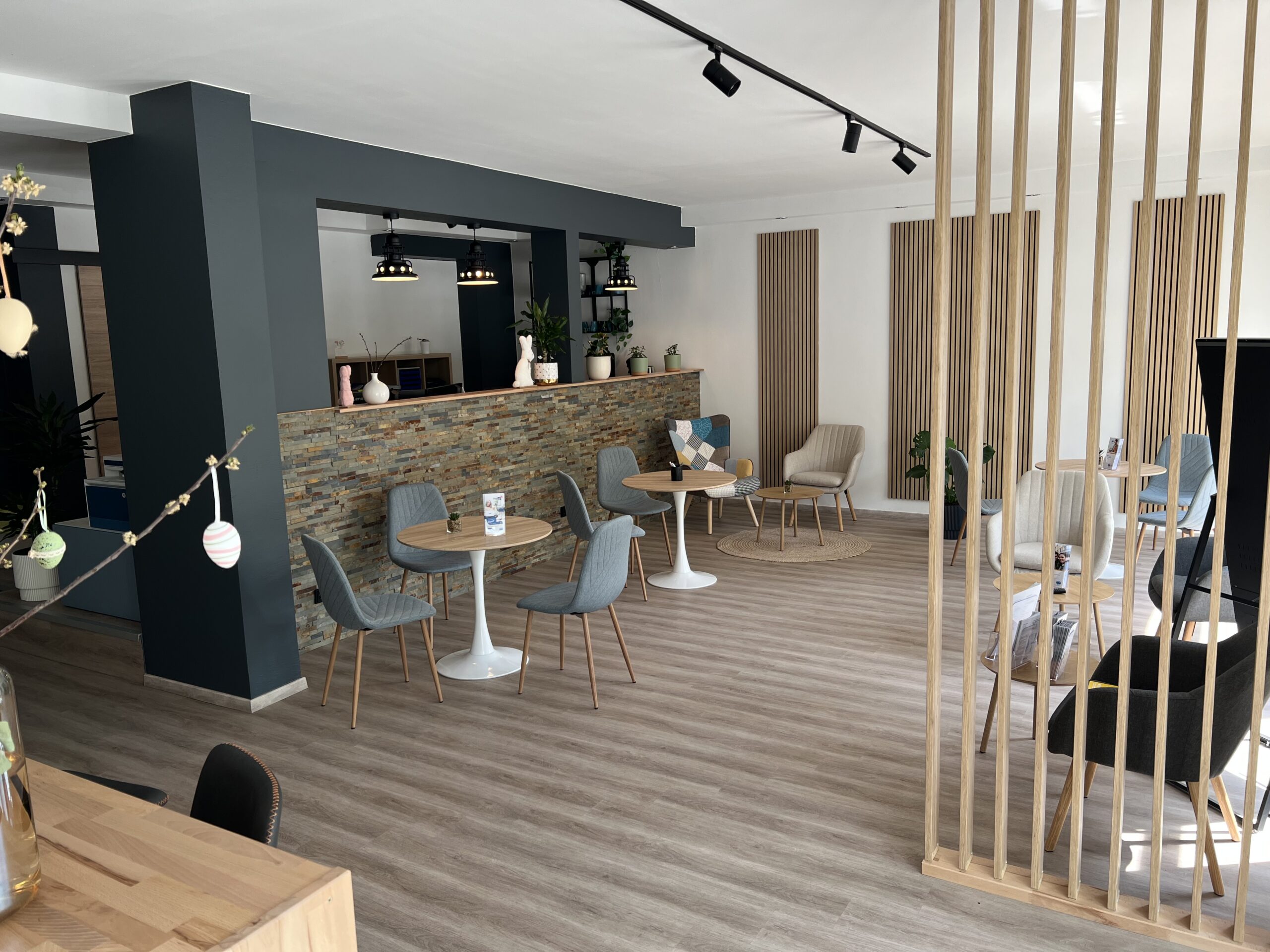 DigiUp Strausberg - Ein digitaler Ort für alle! - Moderner, offener Raum mit gemütlicher Sitzecke, runden Tischen und stilvoller Holz- und Steinwandgestaltung.